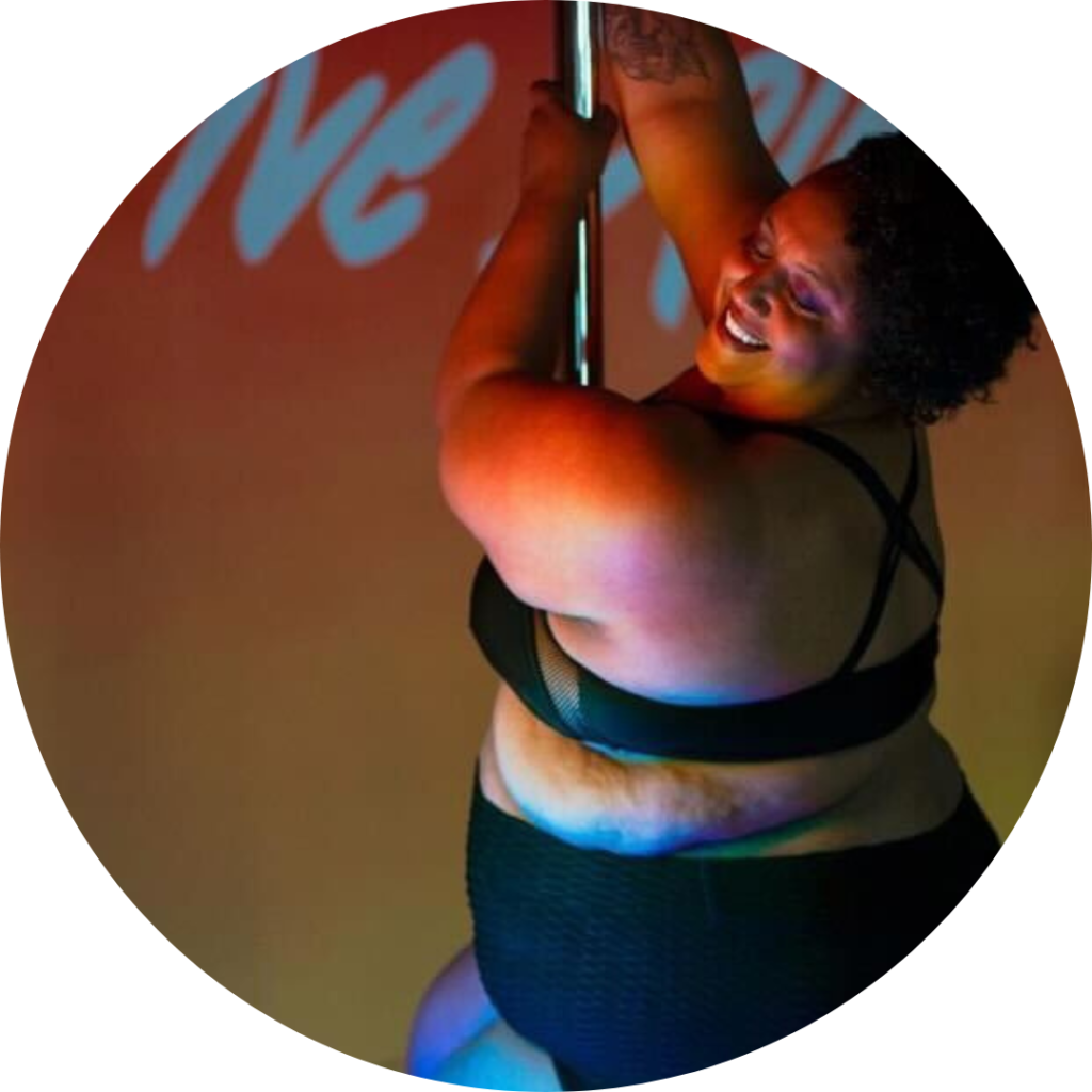 Anna smiles toward the camera while holding the pole with both hands above. They are faintly basked in rainbow lighting.