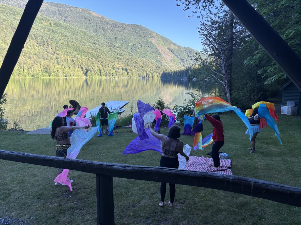 Campers near the lake dancing with colorful silk fans.