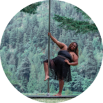 Sydney doing a pole pose with one leg hooked against a backdrop of trees outside.