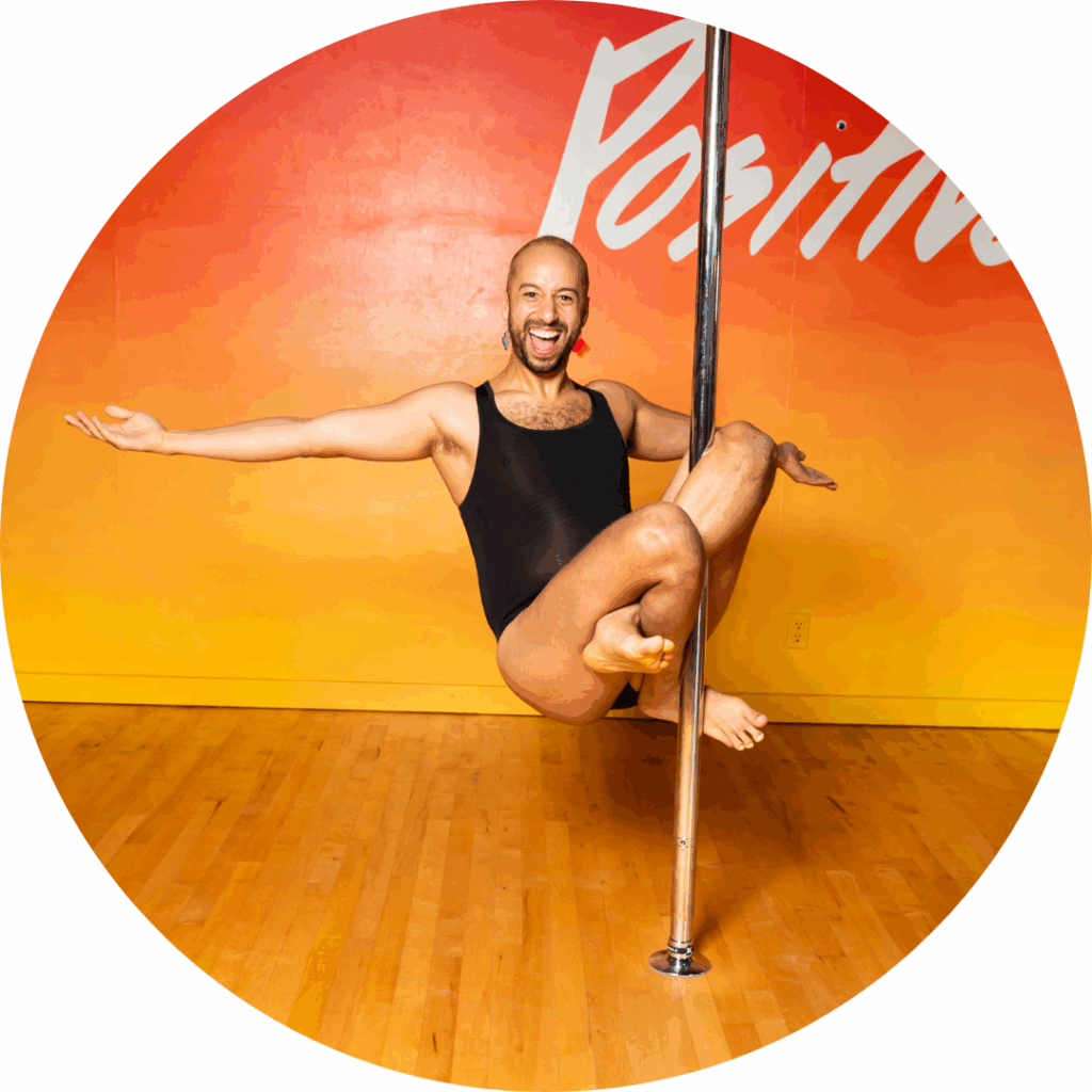 TJ doing a remi sit on the pole against an orange background.