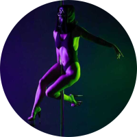 Kenni doing a pole sit in dramatic dark lighting and a mask on.